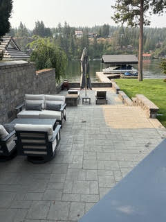 Large paver patio with lounge furniture before cleaning, the surface uneven in tone with a paler weathered section mid-frame.